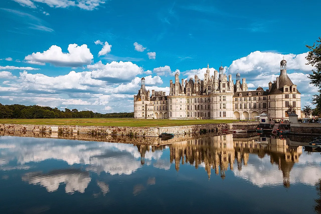 Il castello di Chambord specchiato nell’acqua del canale sotto un cielo di nuvole bianche